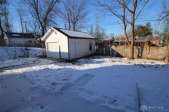 yard layered in snow with an outbuilding, a detached garage, and fence