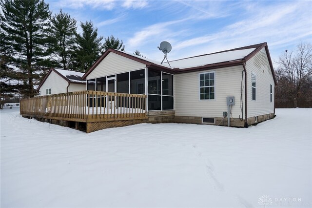 snow covered back of property with a sunroom and a wooden deck