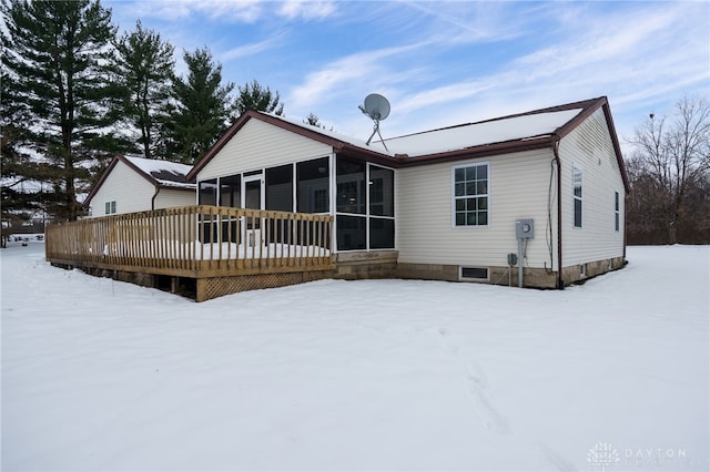 snow covered rear of property featuring a wooden deck and a sunroom