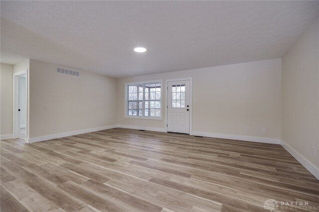 empty room with a textured ceiling and light hardwood / wood-style flooring