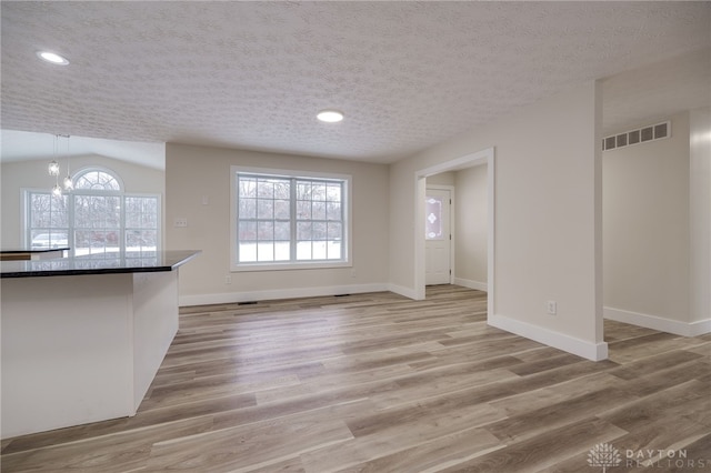 unfurnished living room with lofted ceiling, a chandelier, a textured ceiling, and light hardwood / wood-style floors