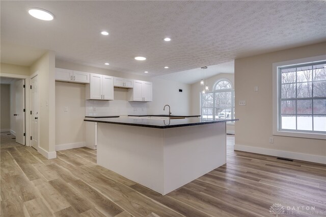 kitchen featuring vaulted ceiling, decorative light fixtures, an island with sink, light hardwood / wood-style floors, and white cabinetry