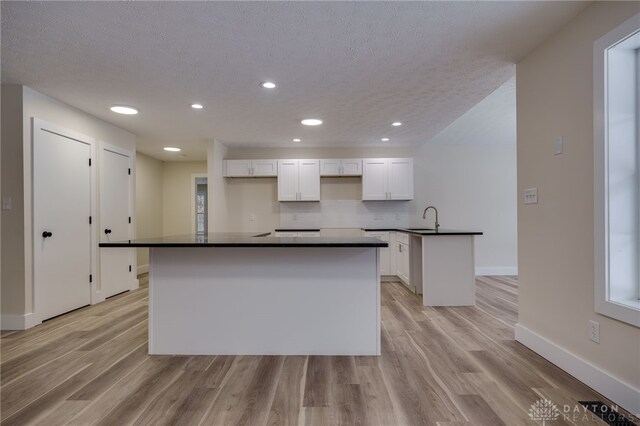 kitchen featuring white cabinets, a center island with sink, tasteful backsplash, and sink