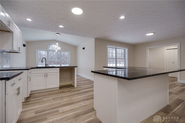 kitchen featuring vaulted ceiling, light hardwood / wood-style floors, pendant lighting, white cabinets, and sink