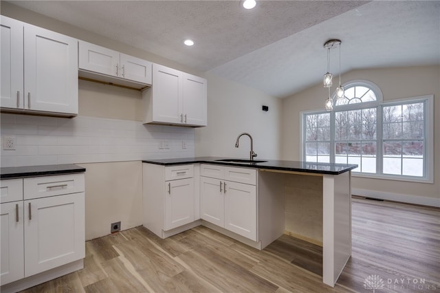 kitchen featuring decorative light fixtures, decorative backsplash, lofted ceiling, white cabinetry, and sink