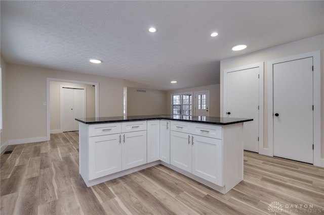 kitchen with white cabinetry, dark stone countertops, a textured ceiling, a kitchen island, and light wood-type flooring