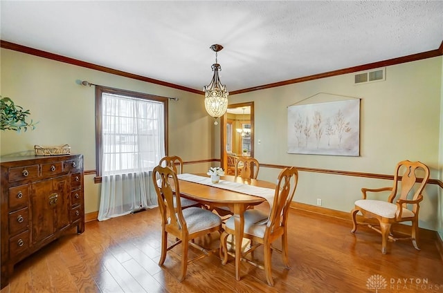 dining space featuring a notable chandelier, crown molding, a textured ceiling, and light hardwood / wood-style floors