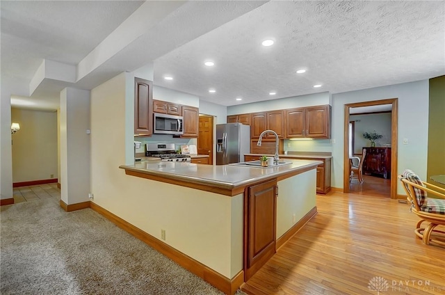 kitchen featuring a textured ceiling, stainless steel appliances, sink, kitchen peninsula, and light wood-type flooring