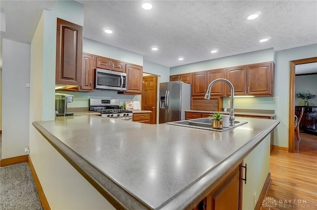 kitchen featuring kitchen peninsula, appliances with stainless steel finishes, a textured ceiling, light hardwood / wood-style flooring, and sink