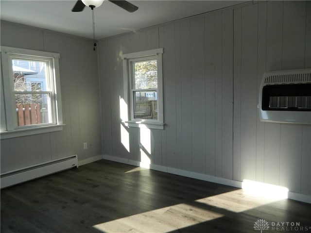 spare room with heating unit, ceiling fan, dark wood-type flooring, wooden walls, and a baseboard heating unit