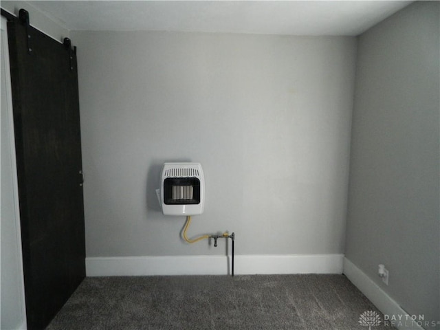 empty room with dark colored carpet, a barn door, and heating unit