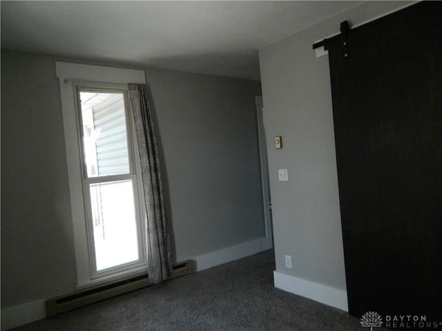 spare room featuring a wealth of natural light, a barn door, dark carpet, and a baseboard heating unit