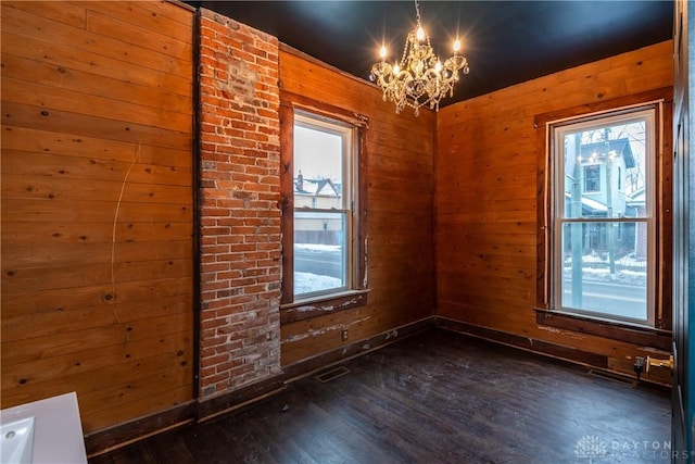 empty room featuring an inviting chandelier, wood walls, and dark hardwood / wood-style floors