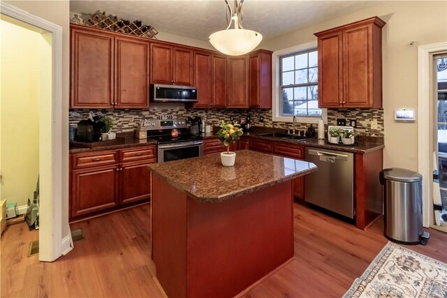 kitchen with stainless steel appliances, sink, light wood-type flooring, hanging light fixtures, and a kitchen island