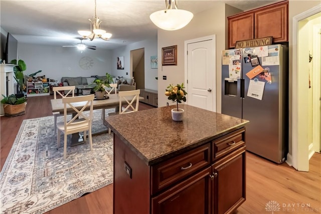 kitchen with stainless steel fridge, ceiling fan with notable chandelier, a kitchen island, and hanging light fixtures