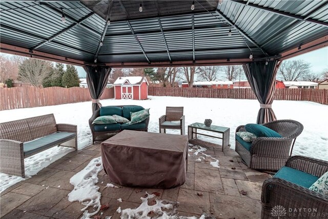 snow covered patio featuring a gazebo, a storage unit, and an outdoor living space