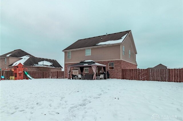 snow covered back of property with a playground and a gazebo