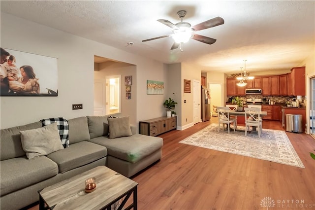 living room with ceiling fan with notable chandelier, a textured ceiling, and light wood-type flooring