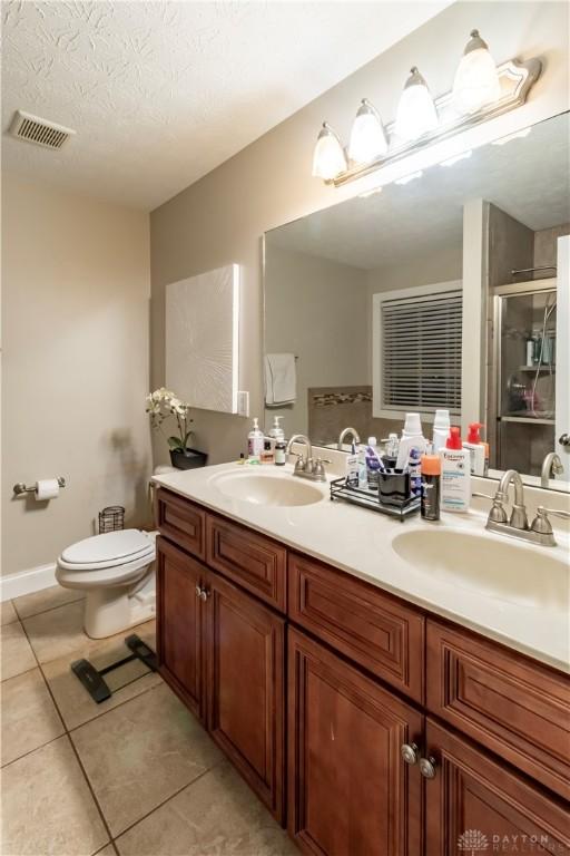 bathroom featuring tile patterned flooring, toilet, vanity, a textured ceiling, and an enclosed shower