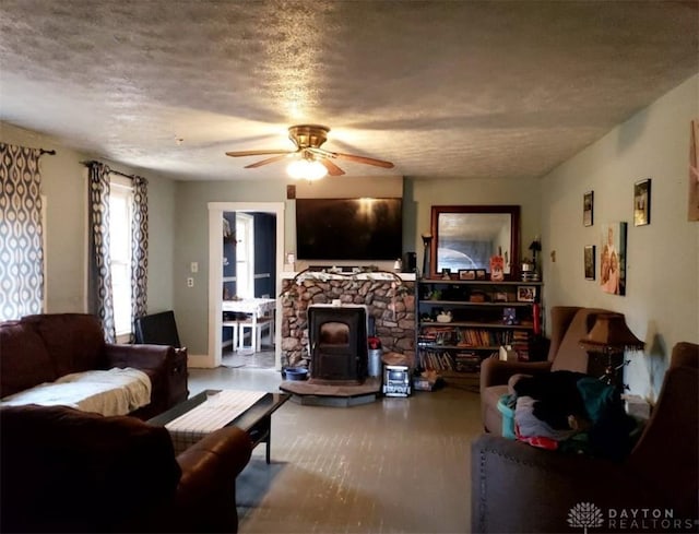 living room with a textured ceiling, ceiling fan, and a wood stove