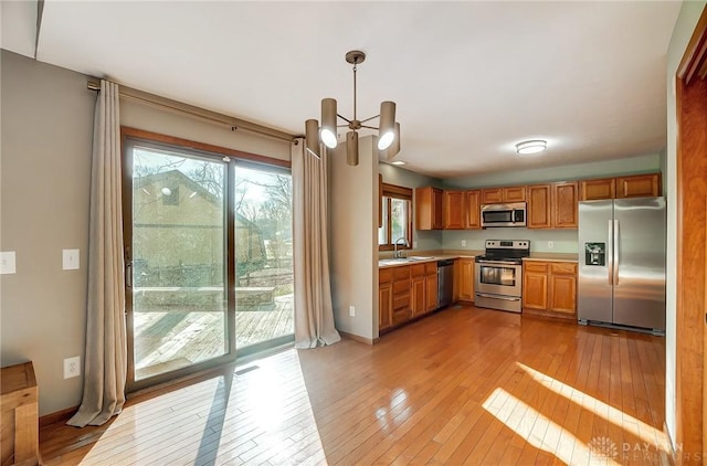 kitchen with an inviting chandelier, appliances with stainless steel finishes, light wood-type flooring, pendant lighting, and sink