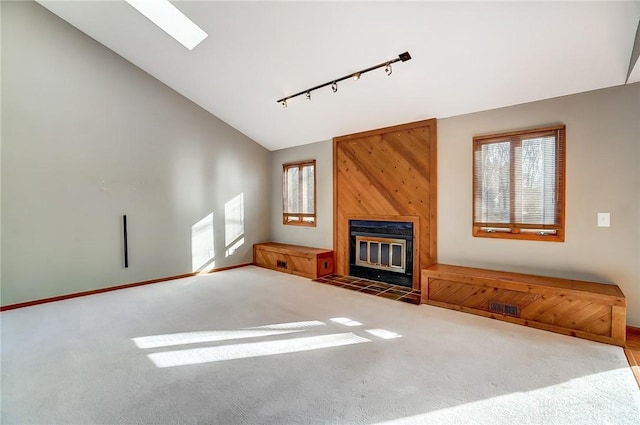 unfurnished living room featuring rail lighting, a large fireplace, vaulted ceiling with skylight, and carpet