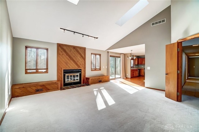 unfurnished living room with light colored carpet, a large fireplace, a skylight, track lighting, and high vaulted ceiling