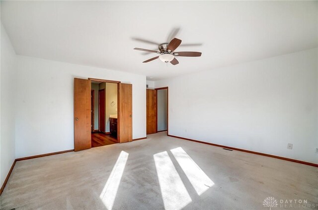 unfurnished bedroom featuring ensuite bathroom, light colored carpet, and ceiling fan