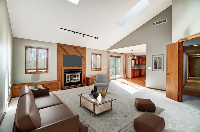 living room with light colored carpet, a fireplace, an inviting chandelier, a skylight, and track lighting