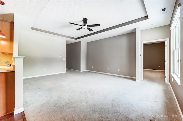 unfurnished living room with ceiling fan, carpet, and a tray ceiling