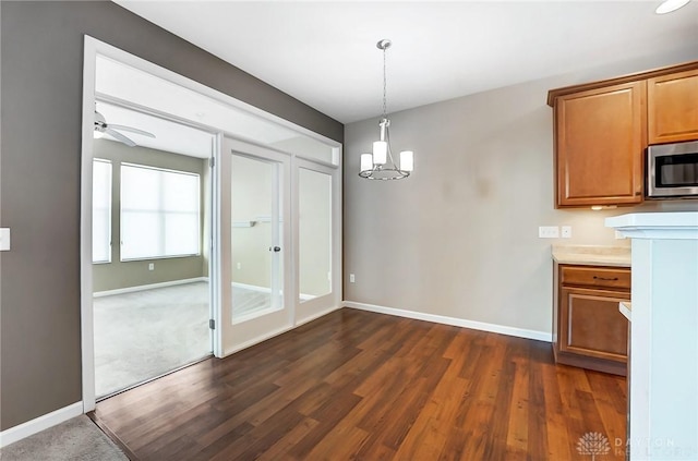 unfurnished dining area featuring ceiling fan with notable chandelier and dark hardwood / wood-style floors