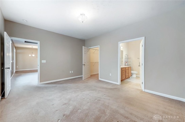 unfurnished bedroom with light colored carpet, connected bathroom, a closet, and a walk in closet