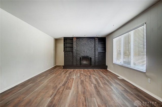 unfurnished living room featuring wood-type flooring and a brick fireplace