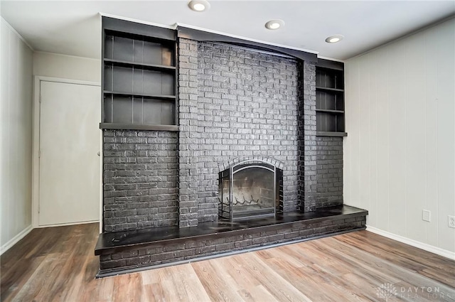 unfurnished living room with built in features, wood-type flooring, and a fireplace