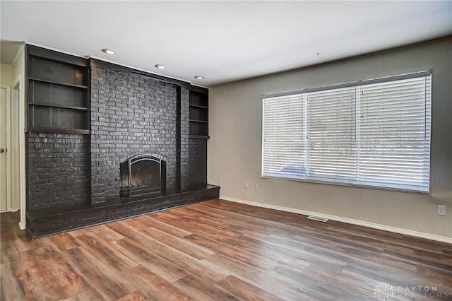 unfurnished living room featuring built in shelves, hardwood / wood-style floors, and a large fireplace