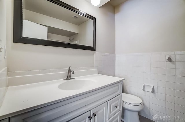 bathroom with toilet, vanity, and tile walls