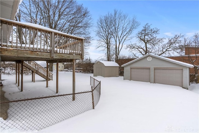 yard layered in snow featuring a garage, a deck, and a storage shed