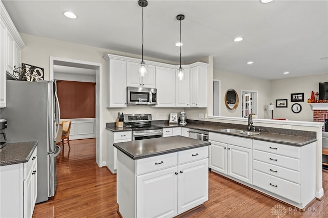 kitchen featuring kitchen peninsula, sink, hanging light fixtures, stainless steel appliances, and white cabinets