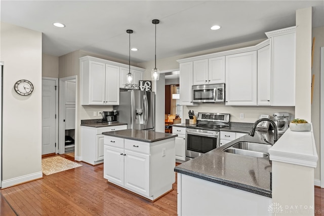 kitchen featuring pendant lighting, appliances with stainless steel finishes, white cabinets, a kitchen island, and sink