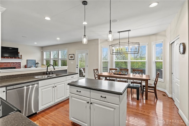 kitchen with a brick fireplace, stainless steel dishwasher, sink, hanging light fixtures, and white cabinets