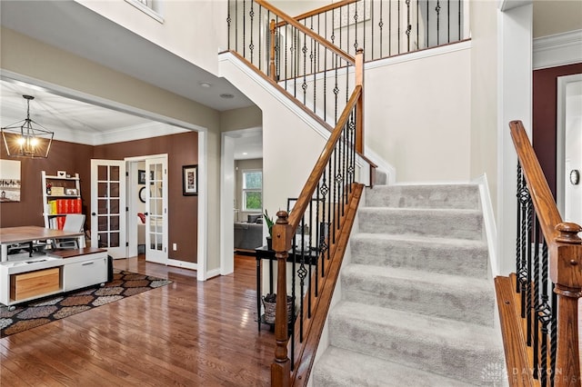 stairway with french doors, an inviting chandelier, ornamental molding, and hardwood / wood-style flooring