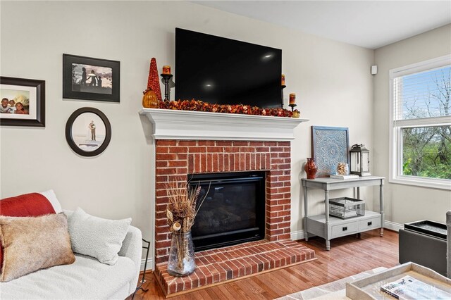 living room featuring a brick fireplace, a healthy amount of sunlight, and hardwood / wood-style floors