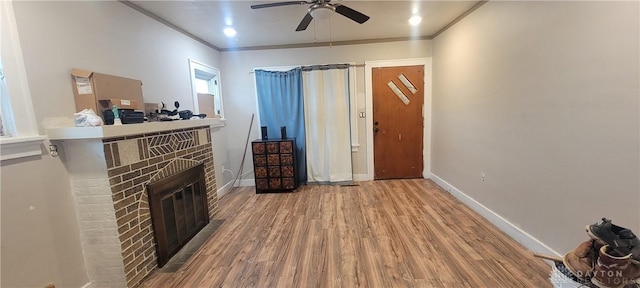 living room featuring a brick fireplace, light hardwood / wood-style flooring, ornamental molding, and ceiling fan