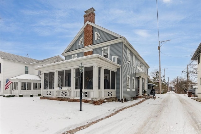 snow covered back of property featuring a sunroom