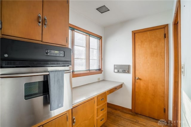 kitchen with built in desk, oven, and light hardwood / wood-style flooring