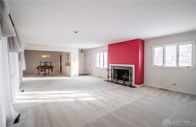 unfurnished living room featuring light colored carpet, a premium fireplace, and a chandelier