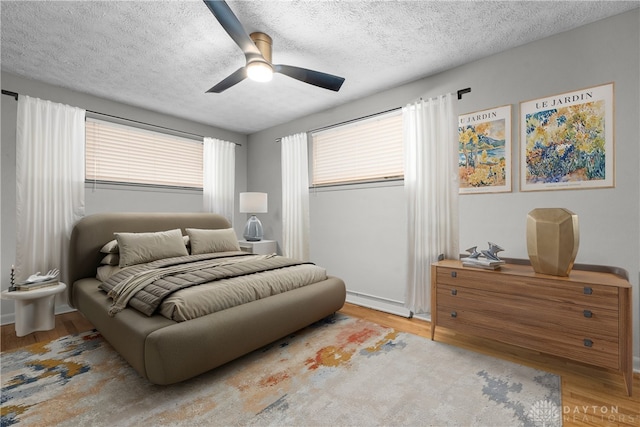 bedroom with a textured ceiling, ceiling fan, light hardwood / wood-style flooring, and multiple windows