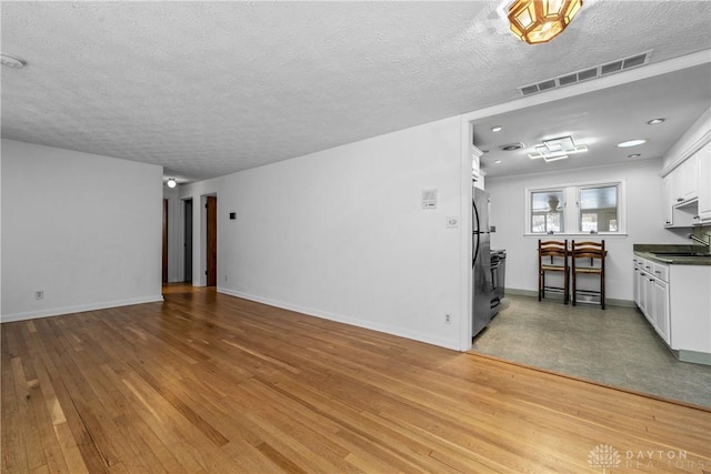 unfurnished living room with light wood-type flooring, sink, and a textured ceiling