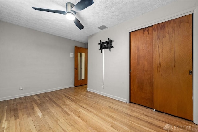 unfurnished bedroom featuring a textured ceiling, ceiling fan, a closet, and light wood-type flooring