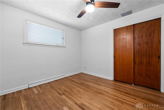 unfurnished bedroom with a baseboard radiator, a textured ceiling, light hardwood / wood-style floors, a closet, and ceiling fan